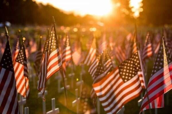 American flags waving in a field at sunset, likely a memorial or cemetery.