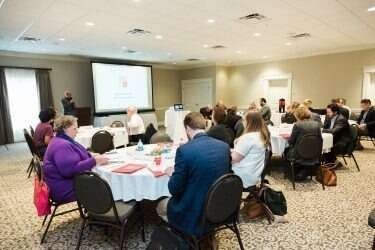People at tables in a conference room, presentation on screen.