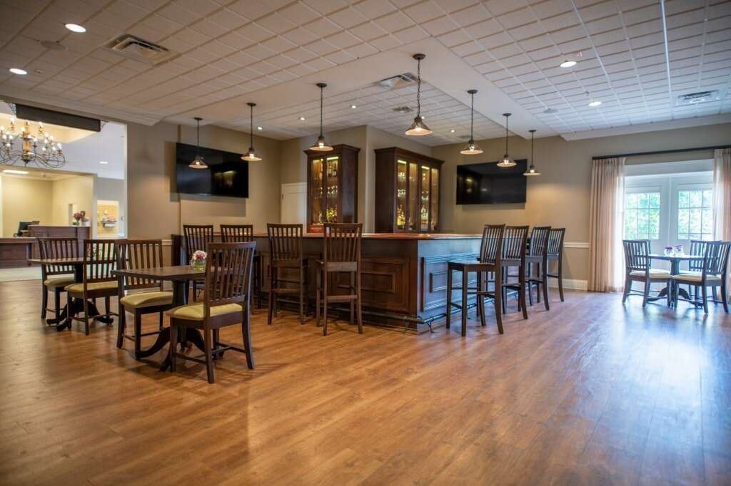 Interior of a bar with wooden floors, bar, tables, and chairs. Two TVs on the wall.