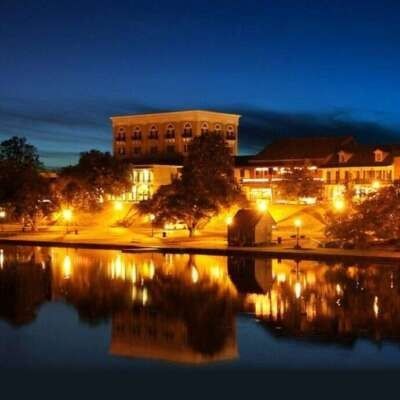 Nighttime view of a city skyline reflected in water, lit by streetlights.