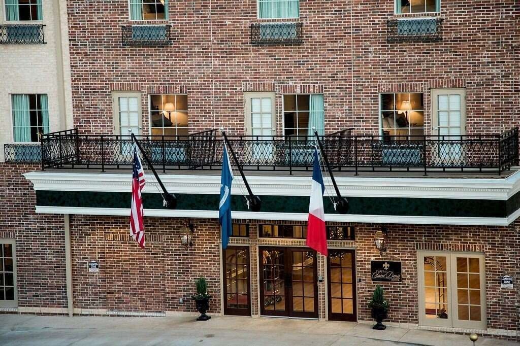 Hotel entrance with brick facade, flags, and balcony.