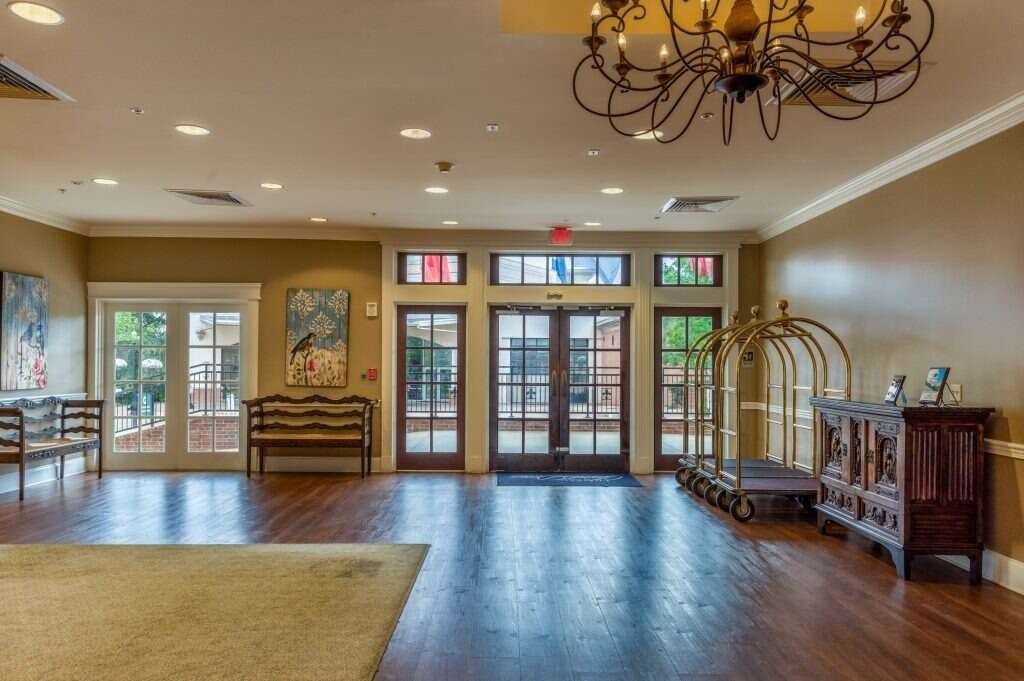 Hotel lobby with wood floors, chandelier, luggage cart, front doors, and entryway rug.