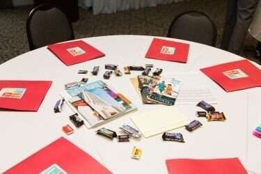 A round table with red folders, brochures, and small items scattered across it, possibly for an event.