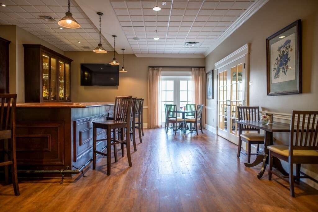 Bar area with wooden floors, bar, stools, tables, and chairs, with a door to an outdoor space.