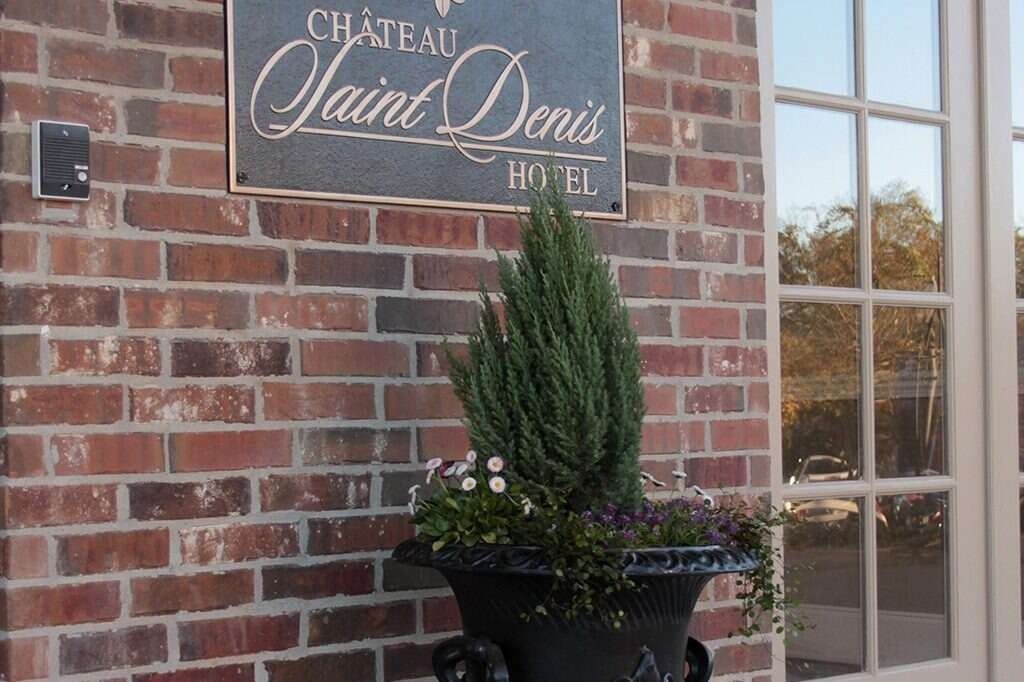 Château Saint-Denis Hotel sign on brick wall next to a window and a planter with greenery.