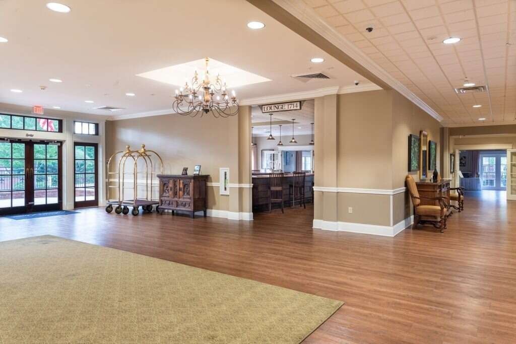 Spacious lobby with wooden floors, a chandelier, and doorways to outdoor areas, a bar, and seating areas.