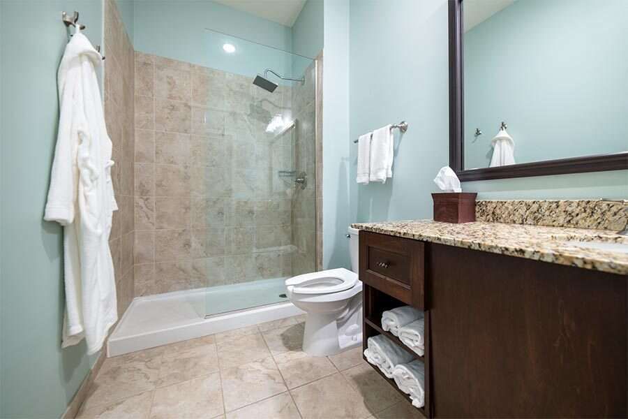 Bathroom with light blue walls, tiled floor, walk-in shower, dark wood vanity, toilet, and white bathrobe.