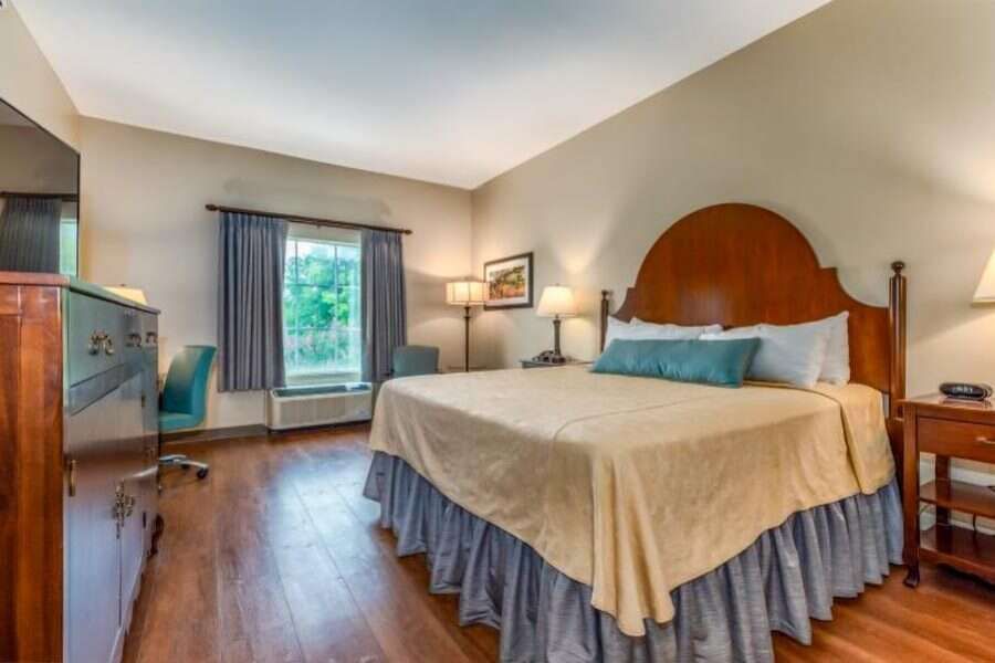 Hotel bedroom with king bed, desk, window, and wooden furniture.
