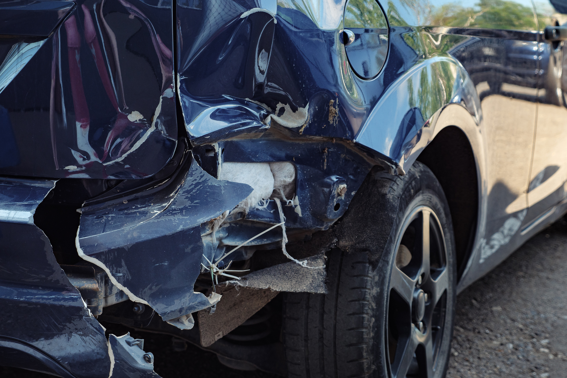 Close-up of damaged blue car after collision, showing dented rear panel, broken bumper.