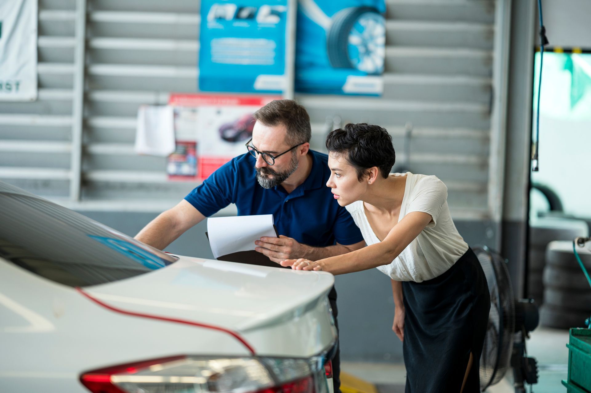 Two people inspecting a car in an auto repair shop.