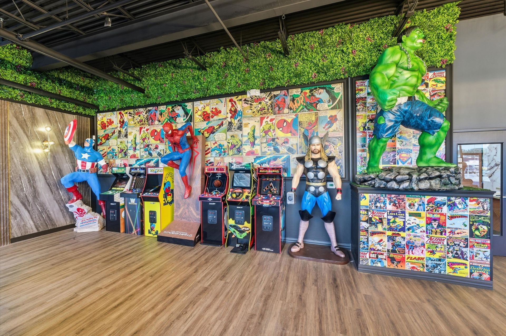 Comic book themed arcade with superhero statues, colorful arcade games, and a green plant wall. Adventure Smiles Dental and Orthodontics -Pasadena