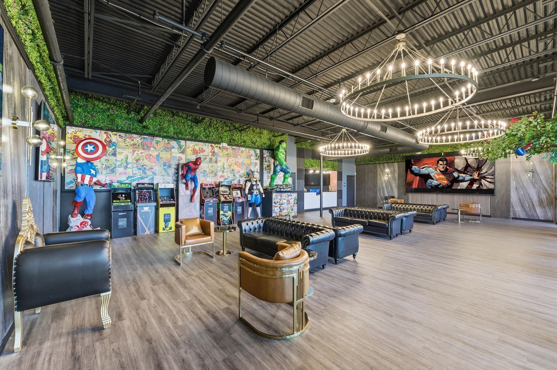 Interior of a lounge with superhero decor, seating, large screen, and decorative lights.