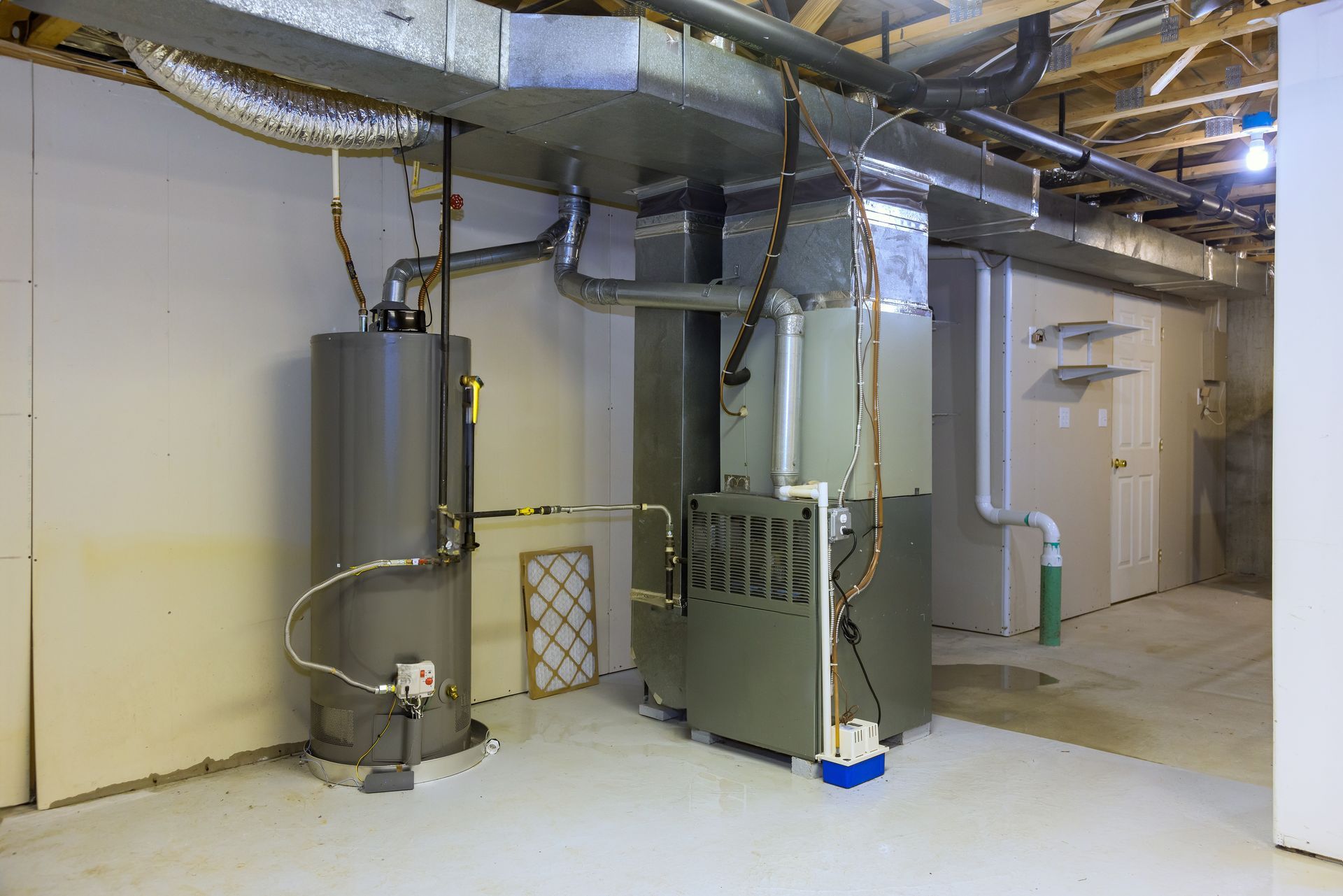 Basement utility room with metal HVAC ducts, water tank, and equipment along a concrete wall.