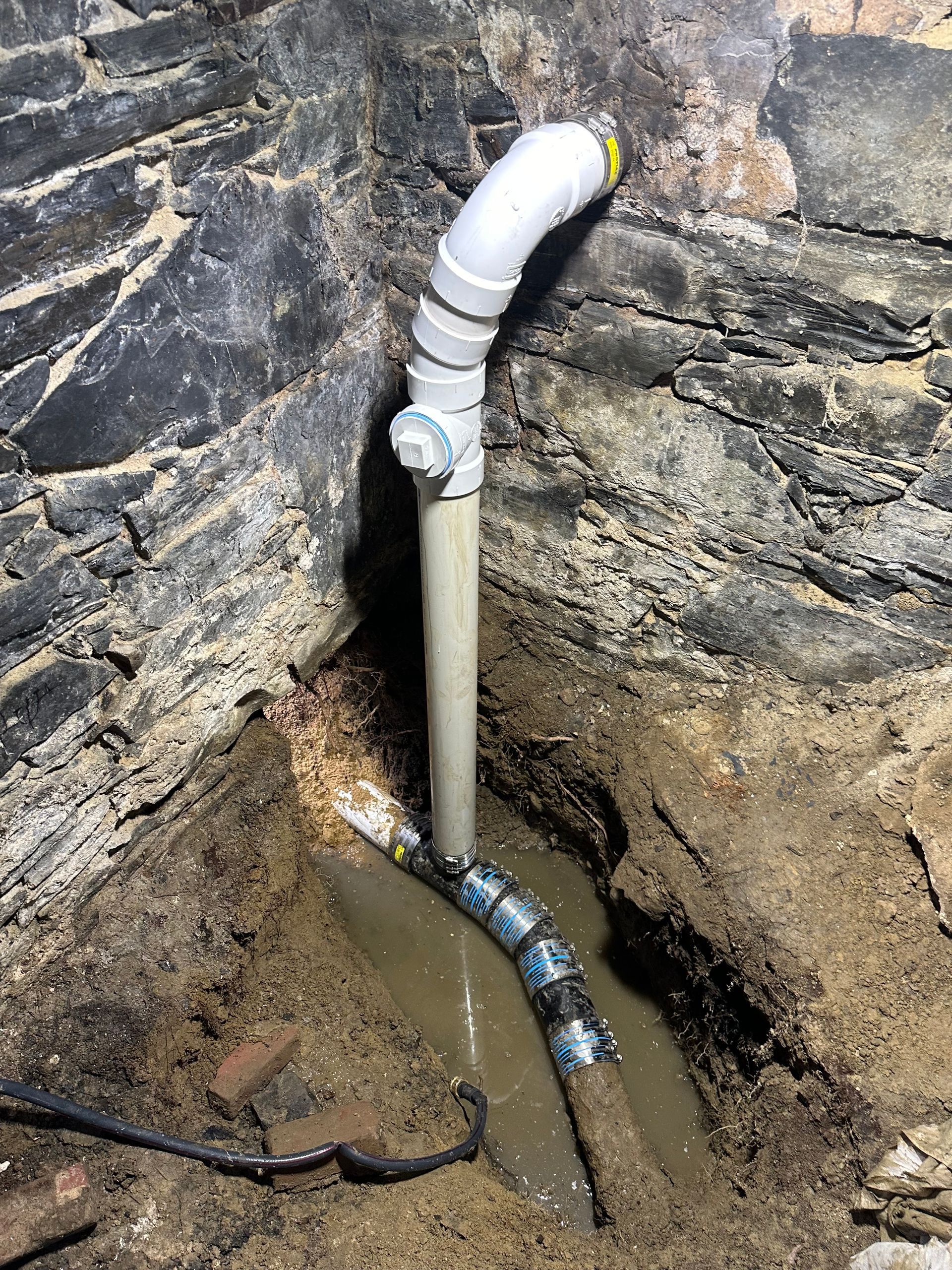 Worker using a drain snake in a concrete basement, with tools and pipes on the floor.