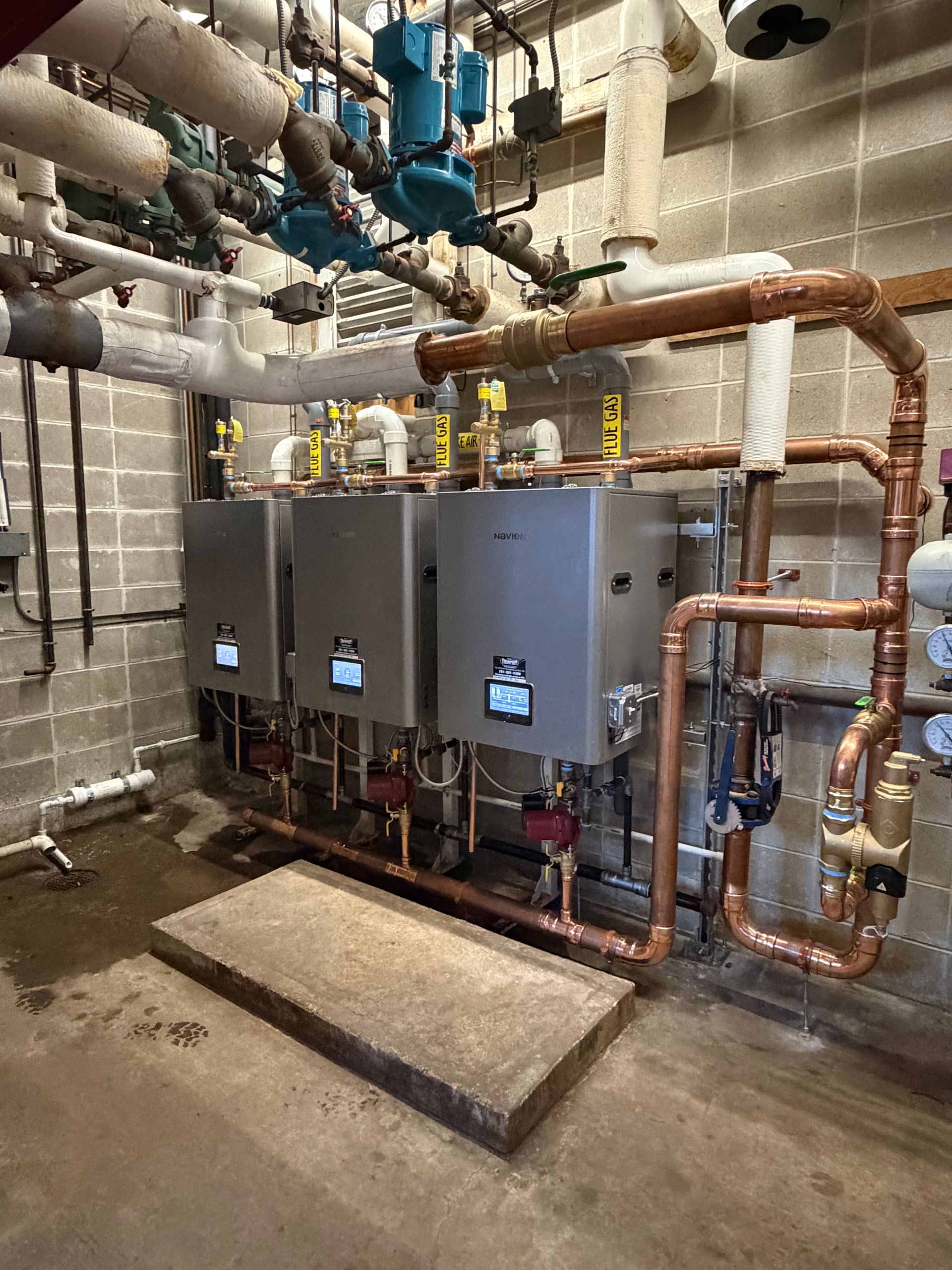 Plumber servicing a white water heater in a basement, adjusting pipes with tools nearby.