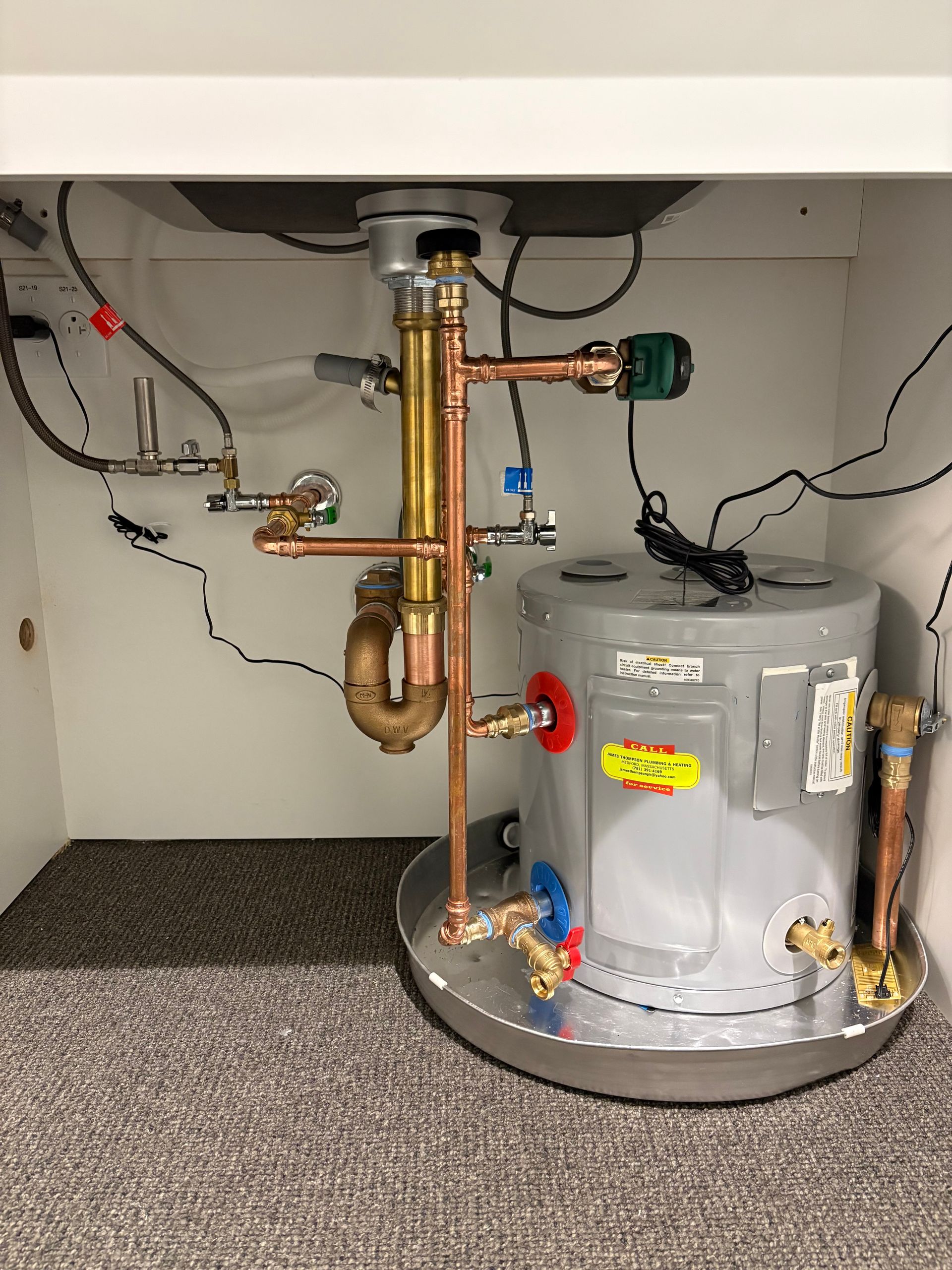 Wall-mounted white boiler with digital control panel in a corner, connected to pipes below