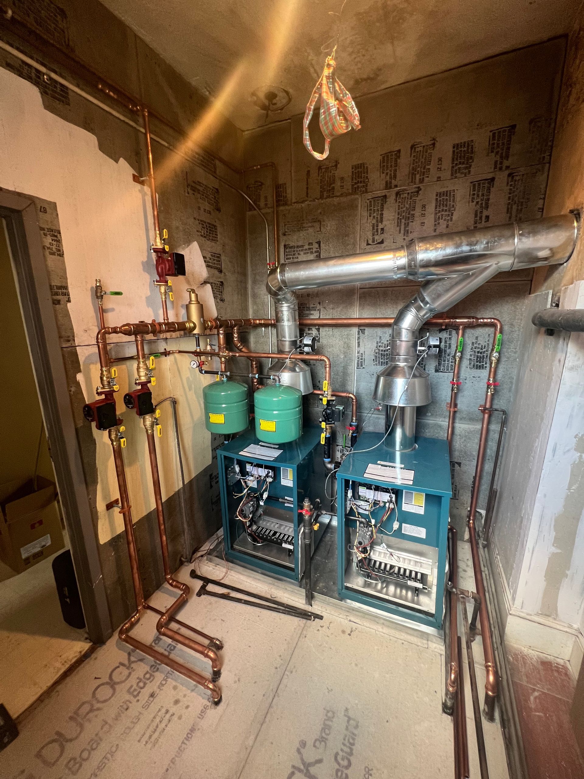 Plumber in blue coveralls working on copper pipes beside a white water heater in a utility room