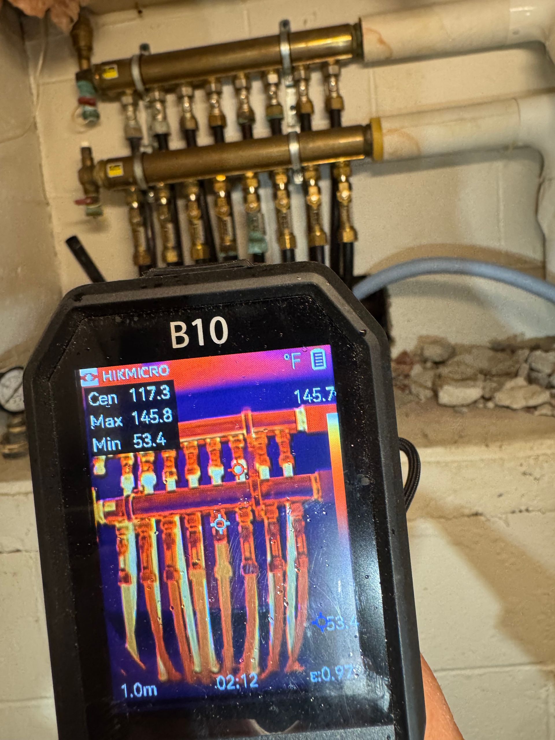 Wall-mounted white boiler with digital control panel in a corner, connected to pipes below