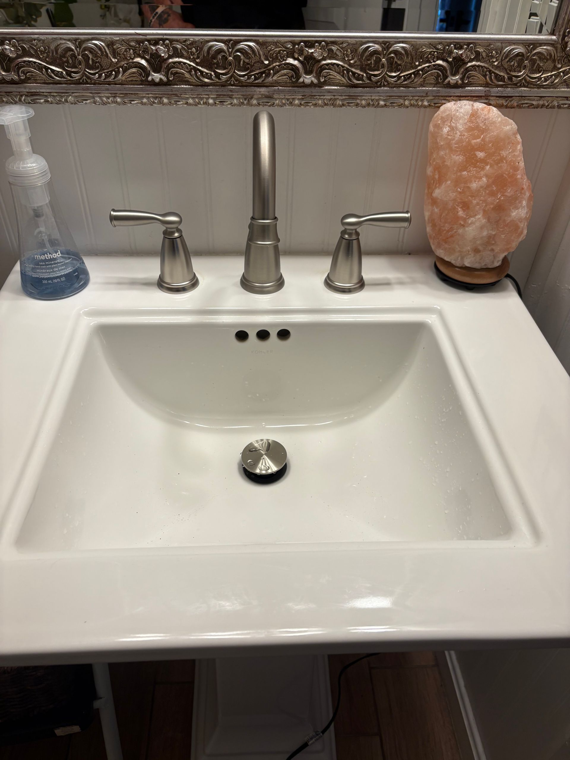 Hands use an adjustable wrench to tighten a metal faucet attached to a wall.