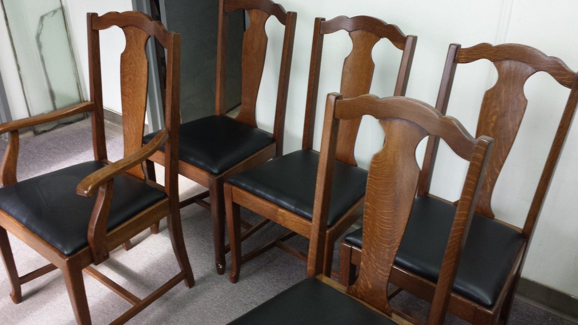 Four wooden dining chairs with black seats arranged on a tiled floor against a wall.