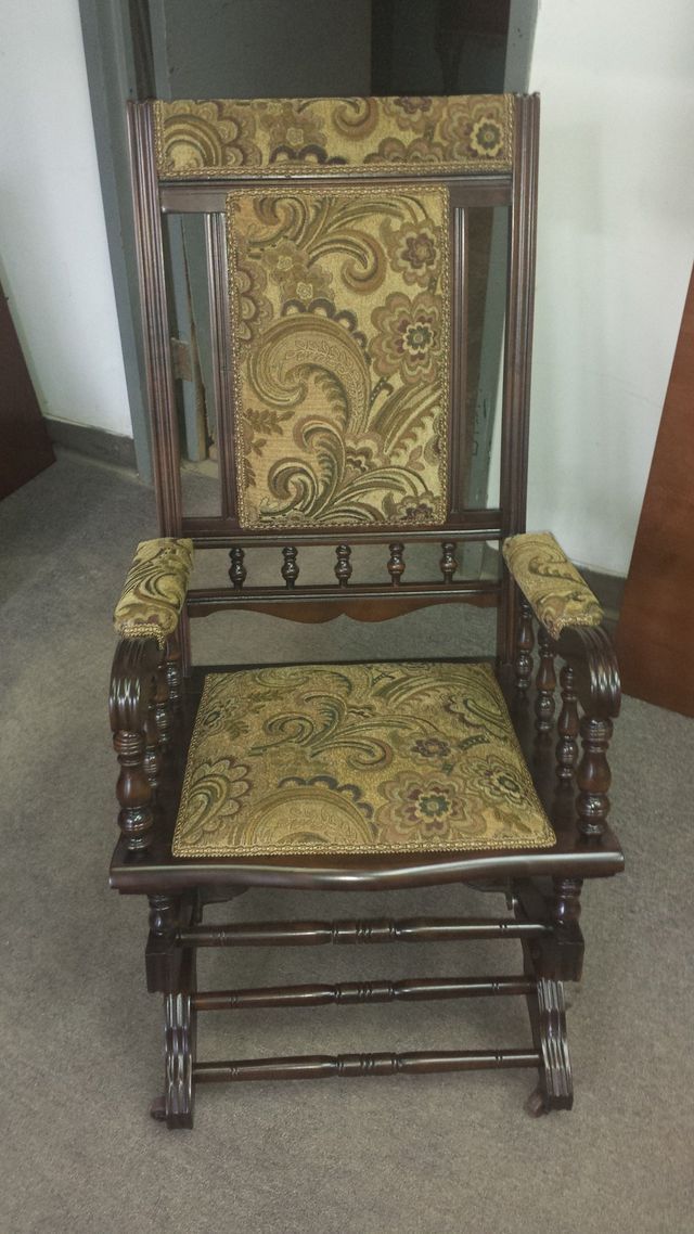 Ornate wooden chair with gold patterned upholstery and carved details against a wall