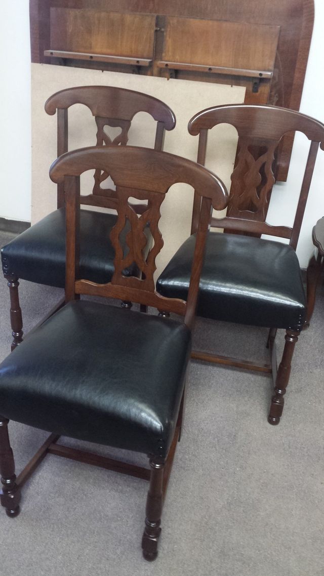 Three wooden dining chairs with dark seats arranged around a table in a carpeted room