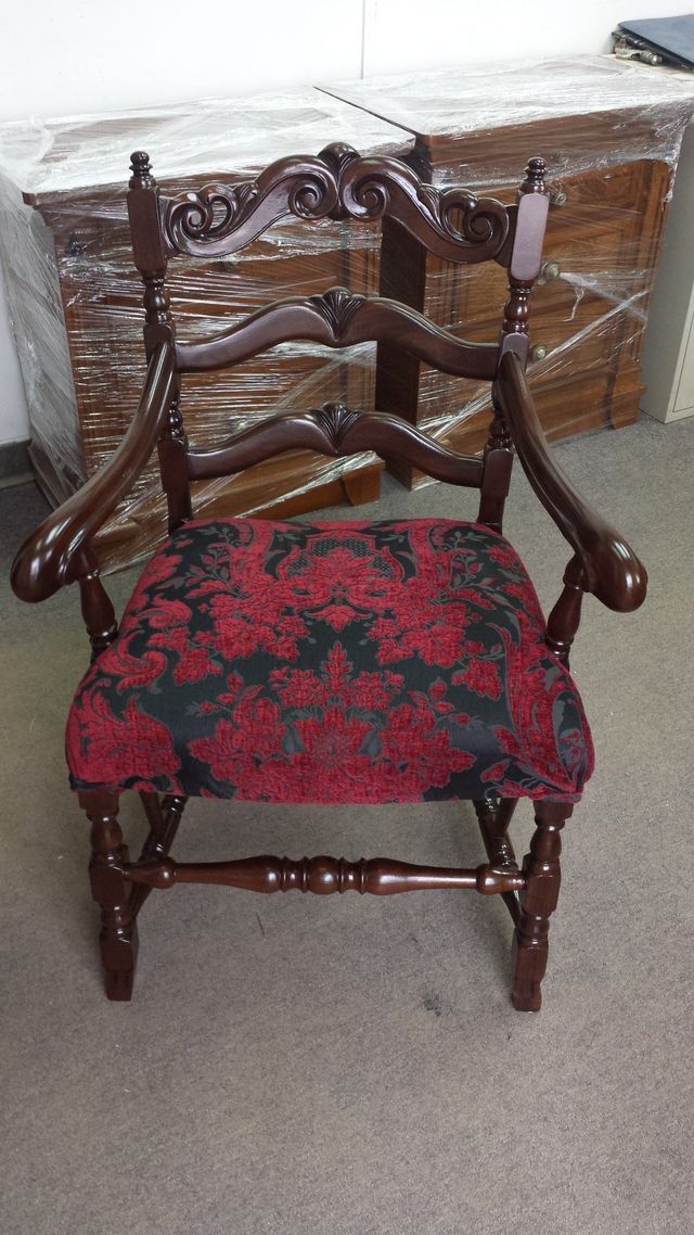 Ornate wooden chair with red and black floral cushion in a room, in front of a wrapped box crate