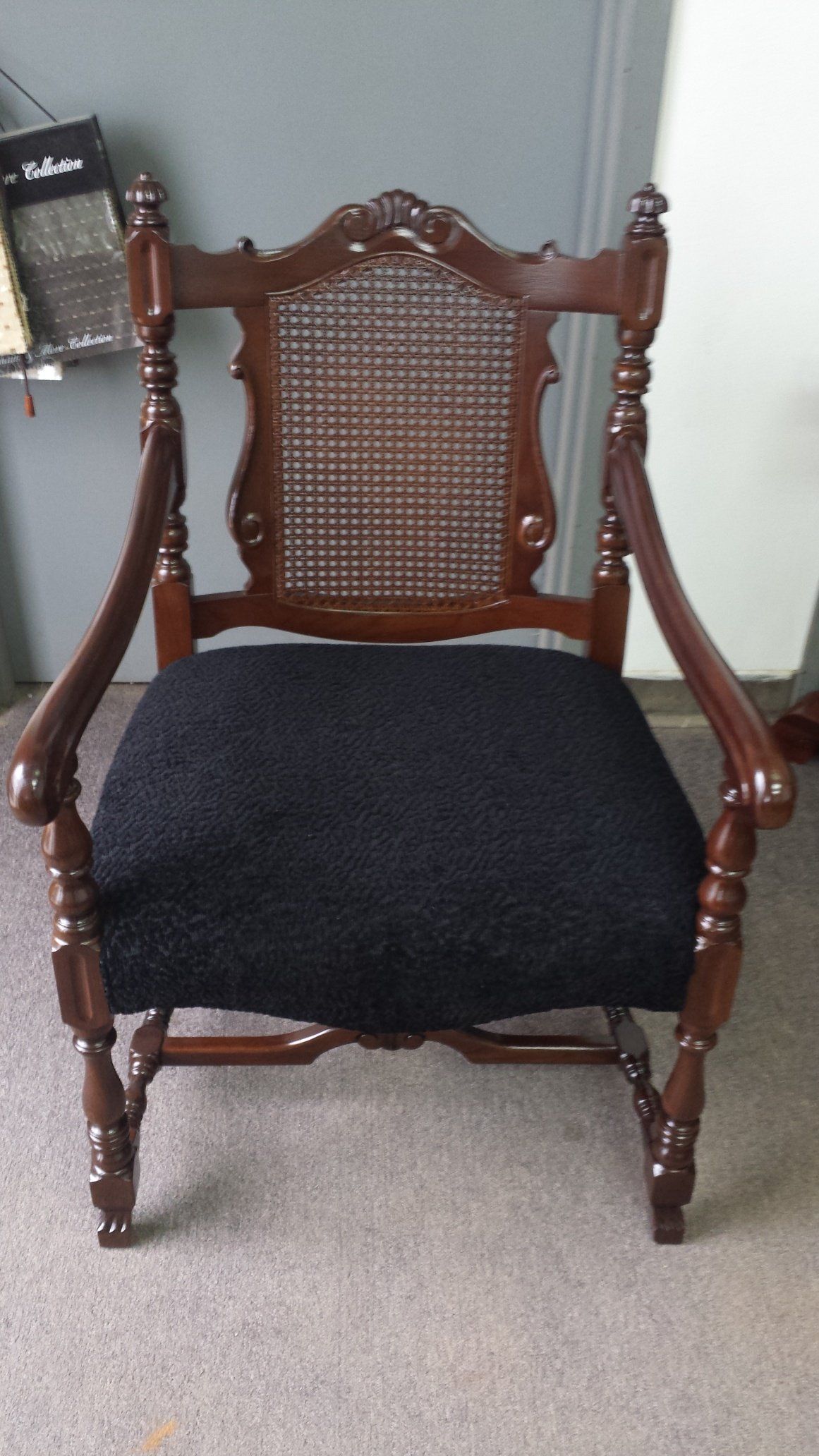 Dark wooden armchair with woven back and black seat cushion on a beige carpet.