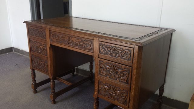 Ornate dark wooden desk with carved drawers against a plain wall on a carpeted floor