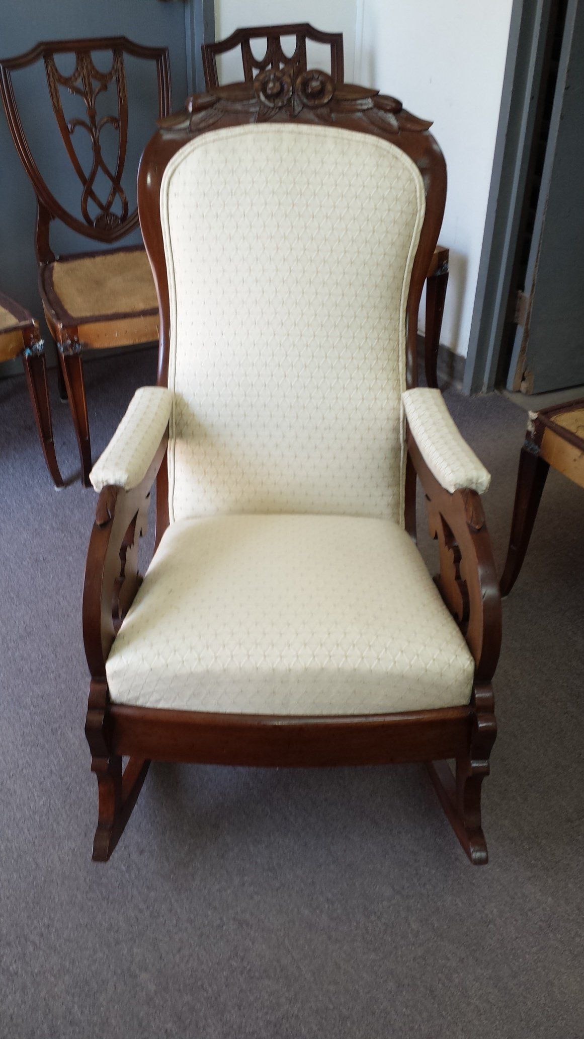Cream upholstered armchair with carved wooden frame in a carpeted room