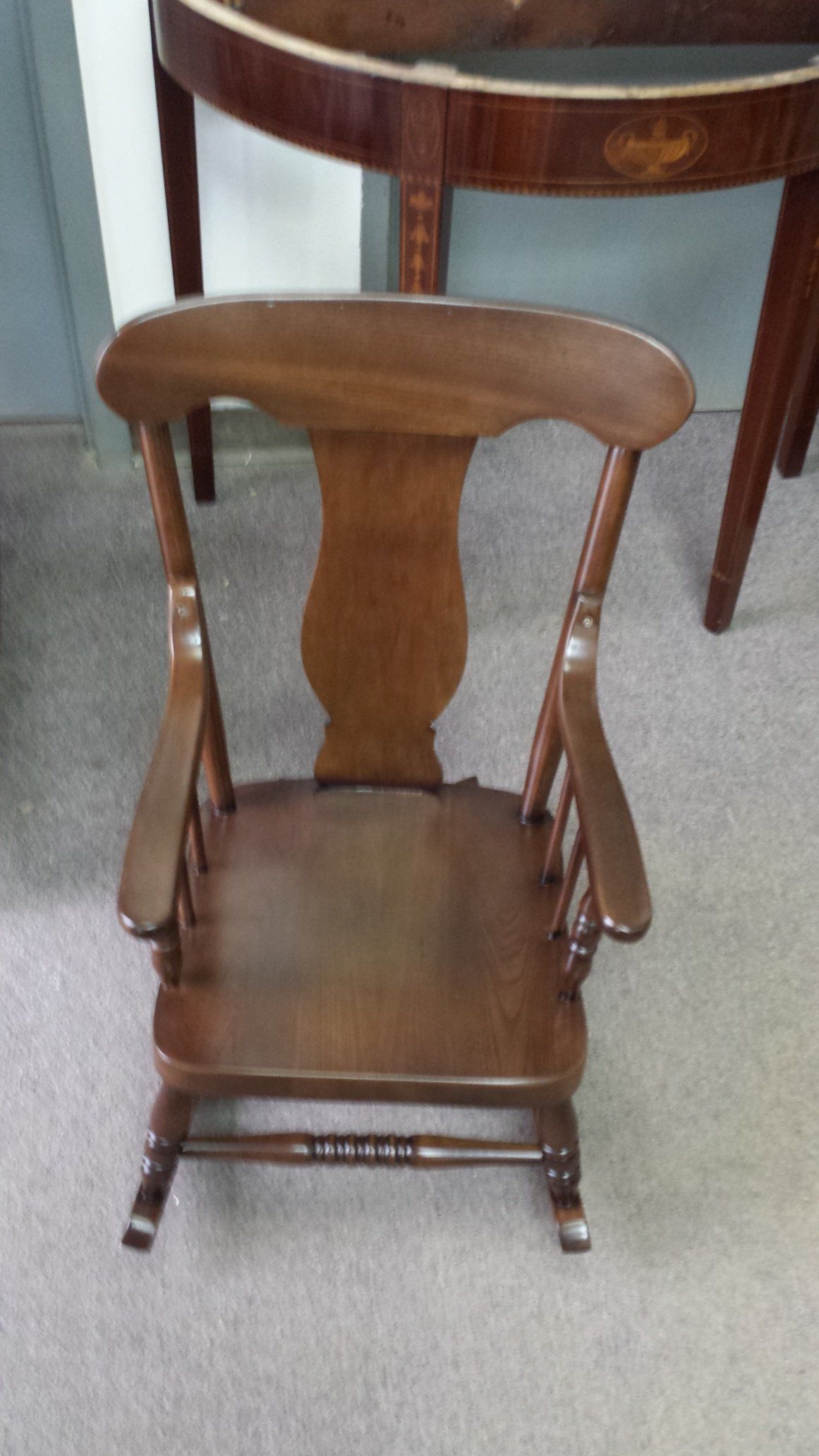 Small wooden chair with curved backrest and spindled arms on a carpeted floor.