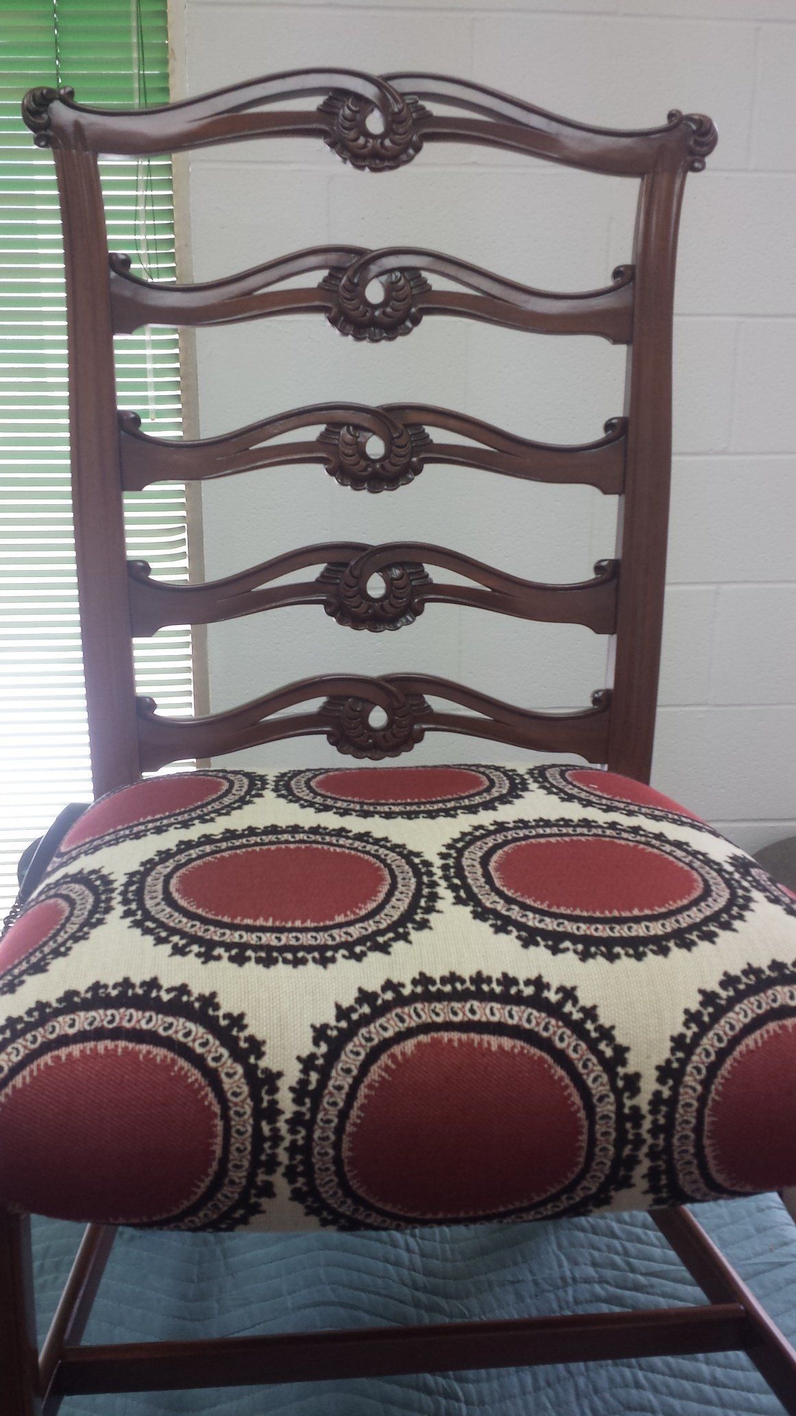 Wooden ladder-back chair with a red, black, and white patterned seat cushion against a tiled wall