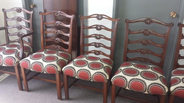 Four matching wooden chairs with red patterned cushions lined up indoors against a wall.