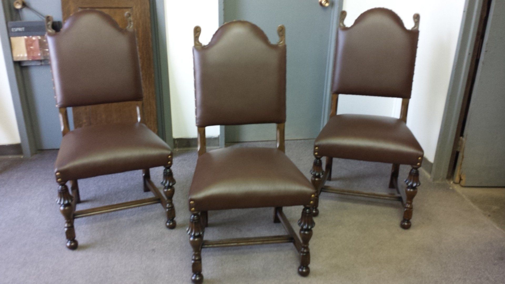 Three ornate brown upholstered chairs arranged in a row on a carpeted floor indoors