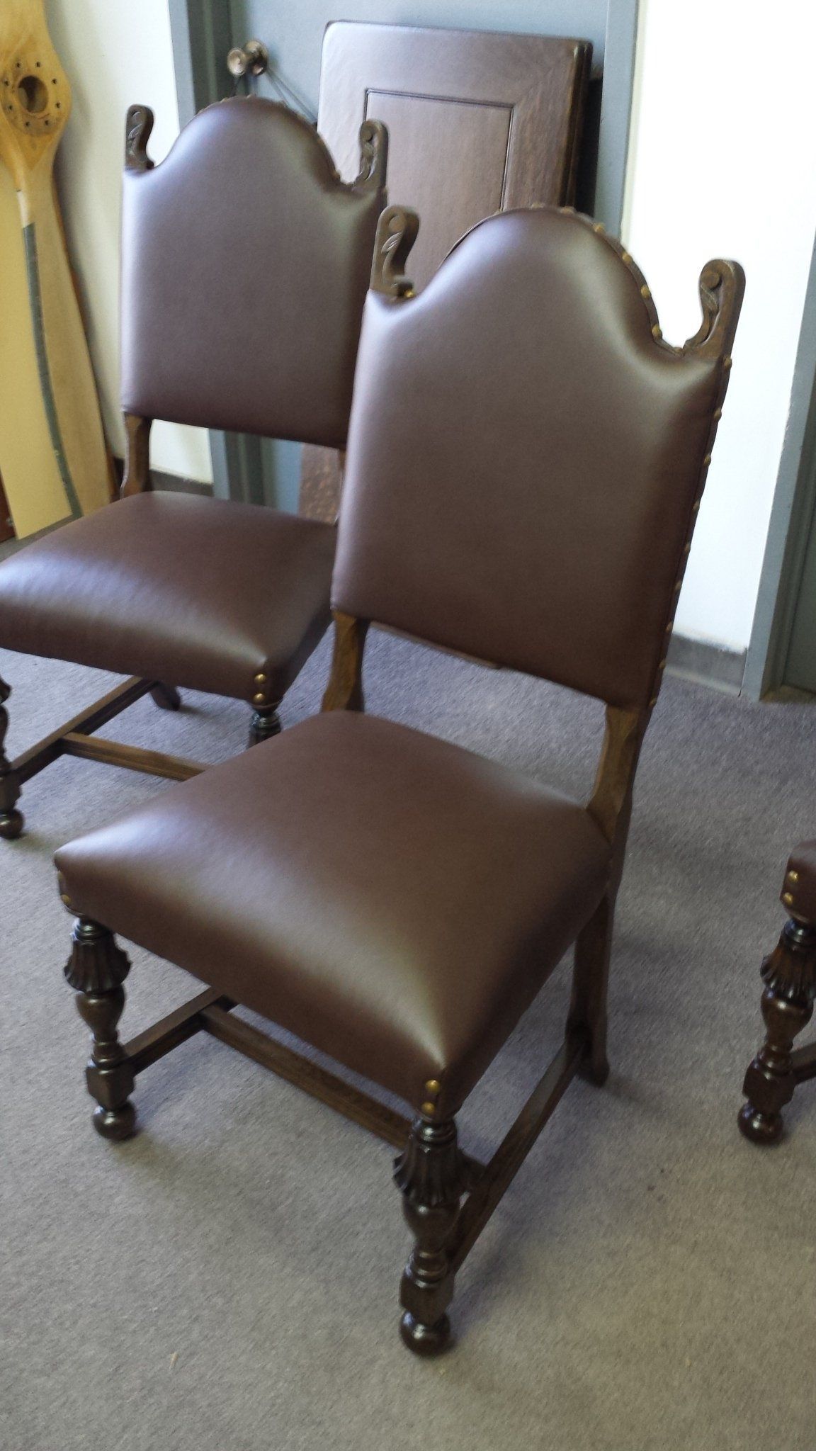 Two brown upholstered dining chairs with carved wooden legs in a carpeted room