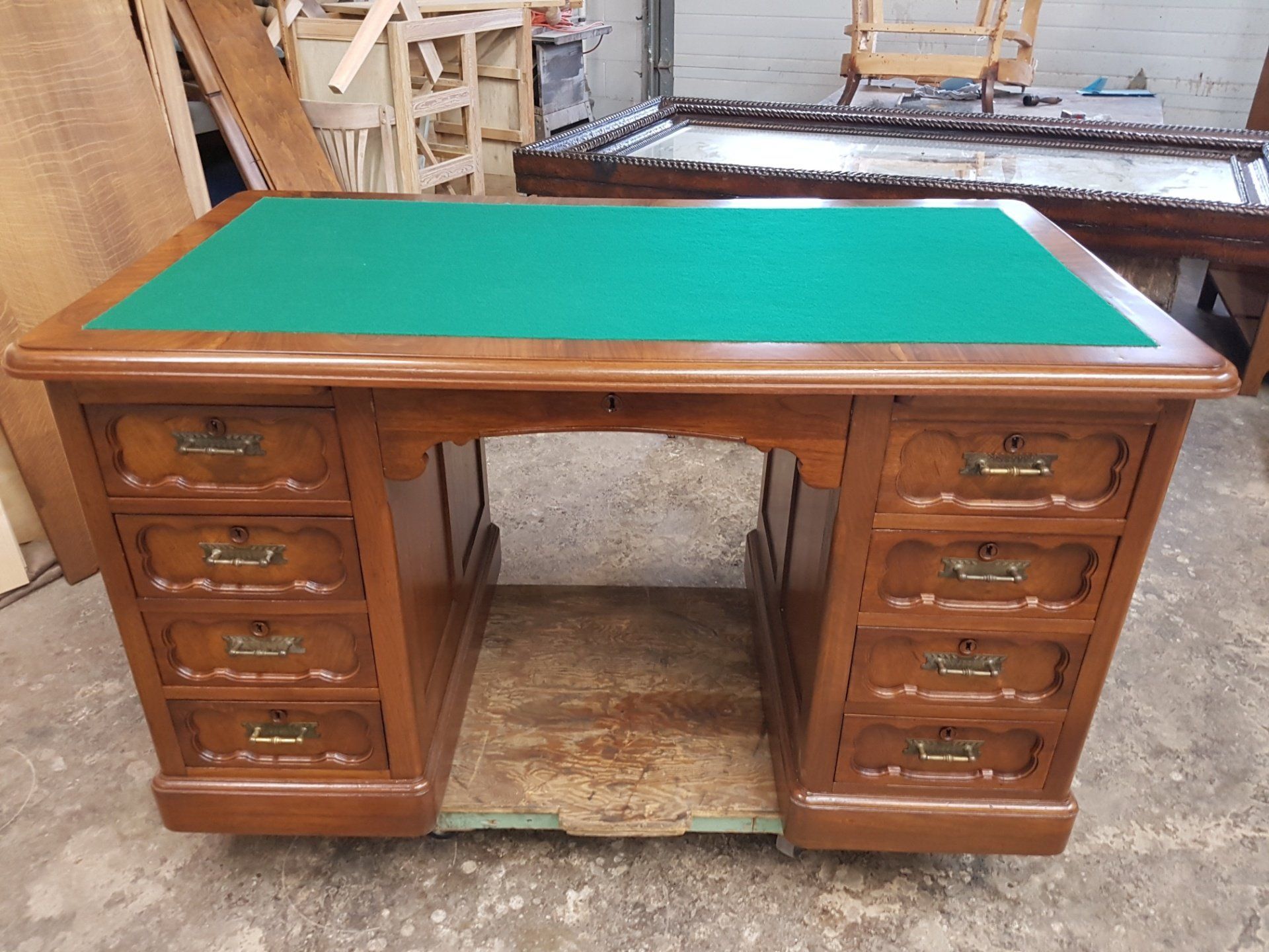 Wooden desk with green felt top and multiple drawers in a workshop.