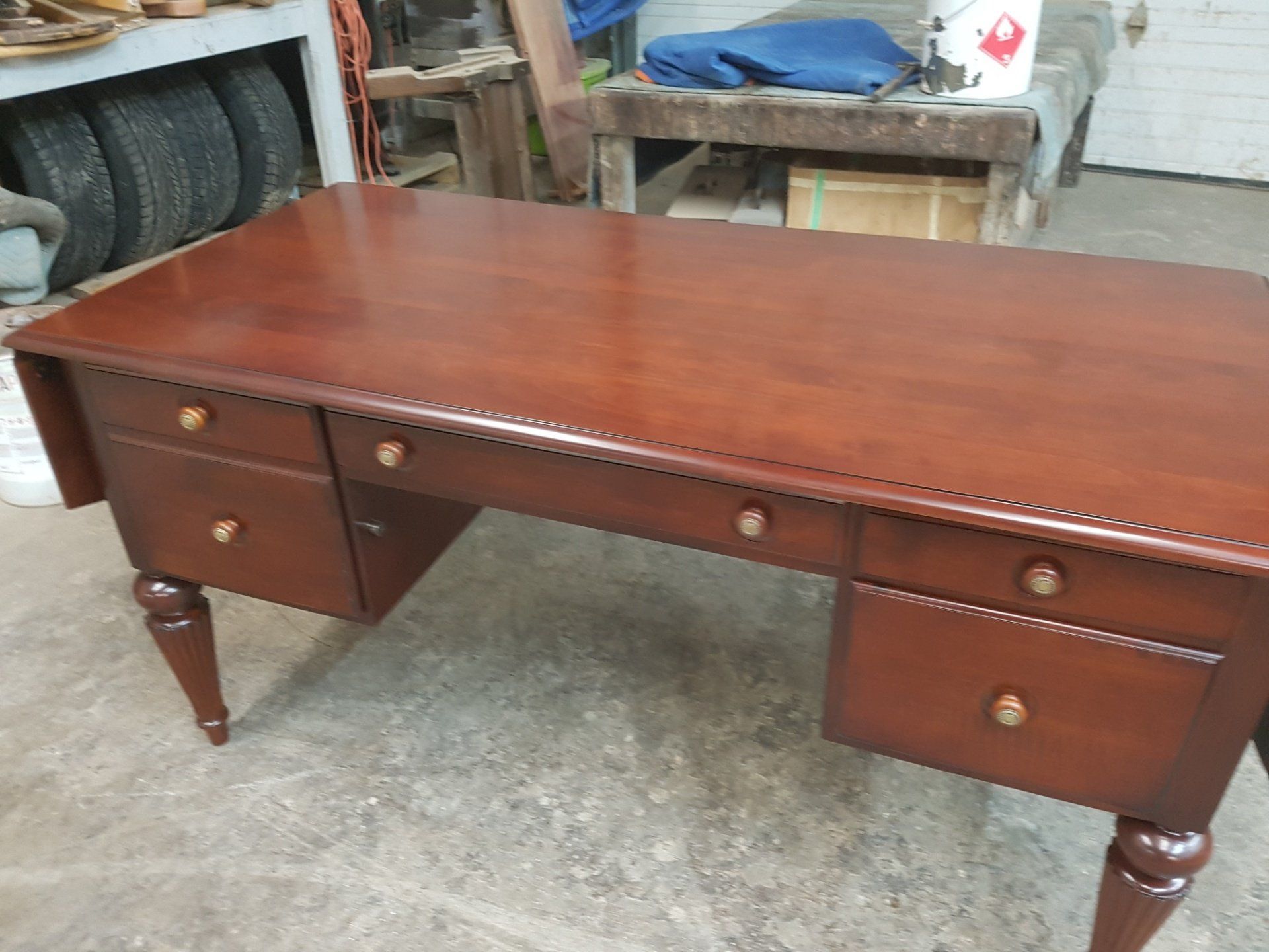 Brown wooden desk with drawers and turned legs in a workshop setting