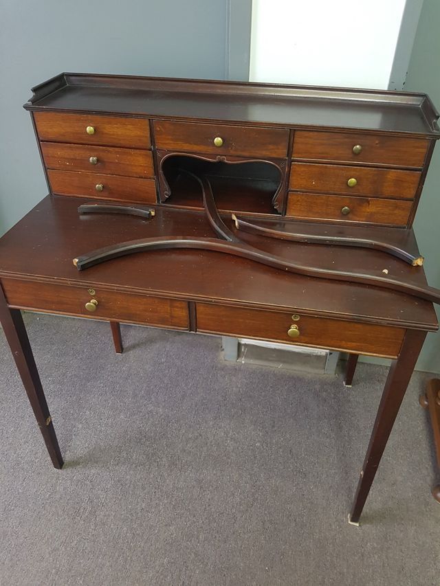 Antique wooden desk with a matching curved chair or bench in a carpeted room