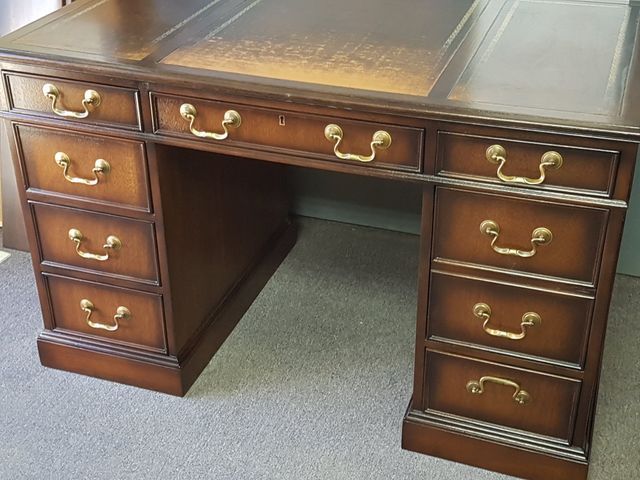 Dark wood executive desk with brass handles and a knee space, shown on carpet indoors