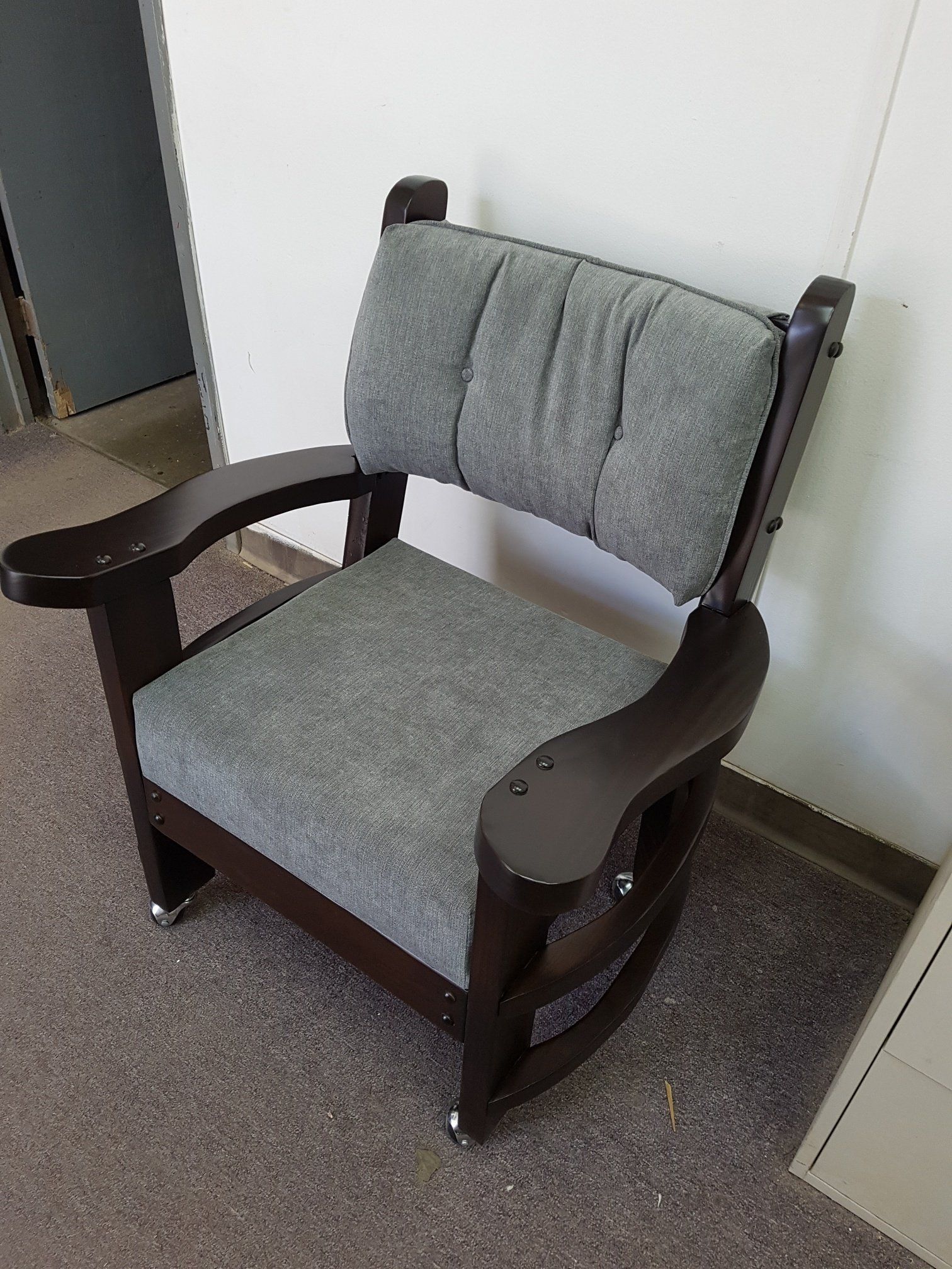 Gray upholstered armchair with dark wooden arms in a hallway against a white wall.