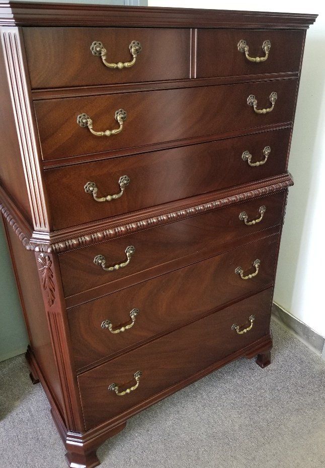 Dark wood dresser with brass handles and six drawers against a white wall on carpet.