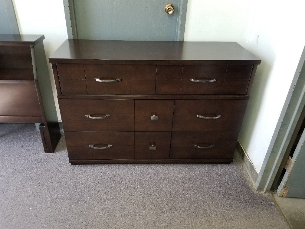 Dark wood dresser with six drawers in a hallway, against a light blue wall.