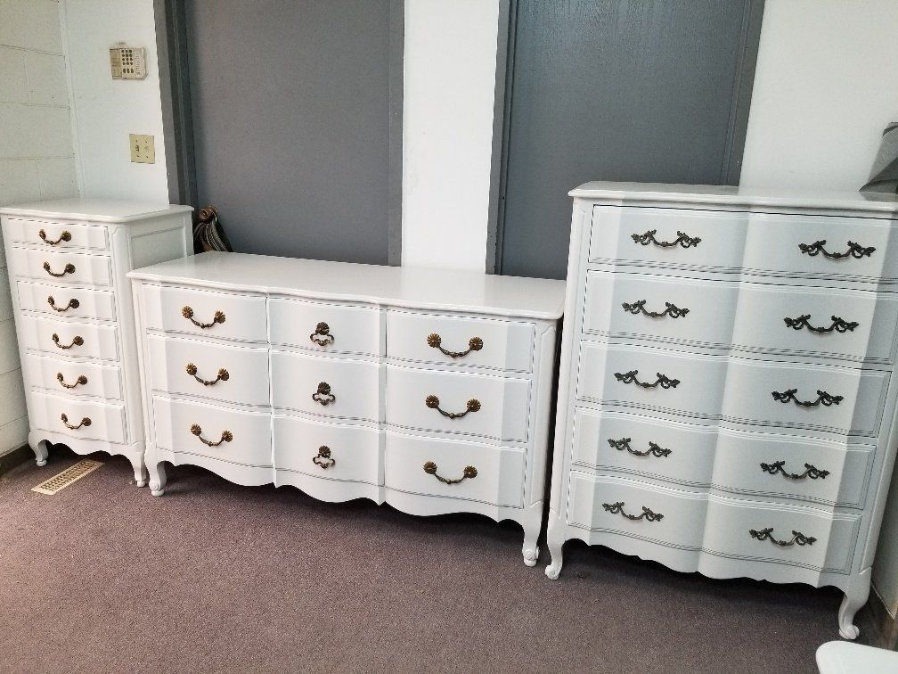 Three white dressers with ornate handles arranged against a wall in a carpeted room.