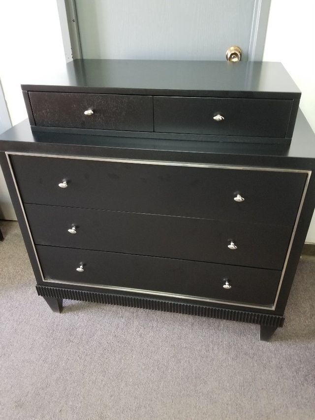 Black dresser with three drawers and two top drawers in a carpeted room.