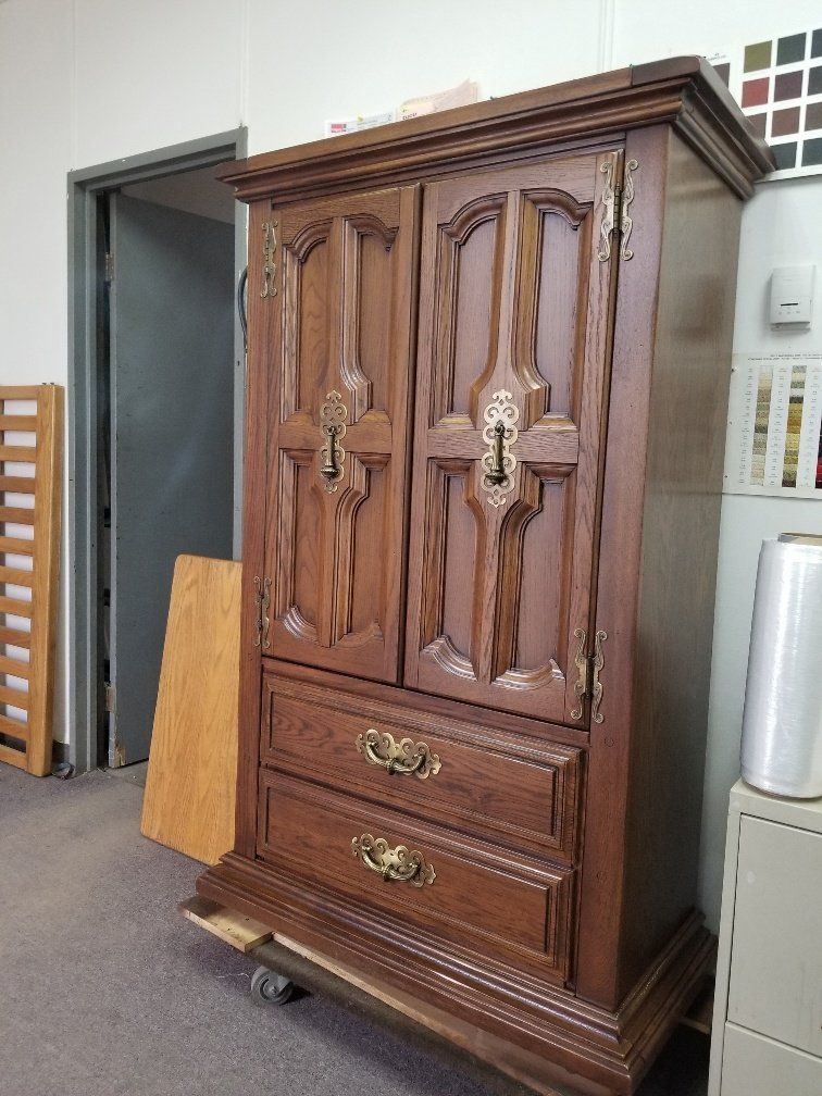 Tall carved wooden wardrobe with ornate handles and two drawers in a room