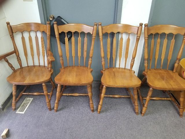 Four wooden chairs with carved backs lined up on a carpeted floor against a wall.