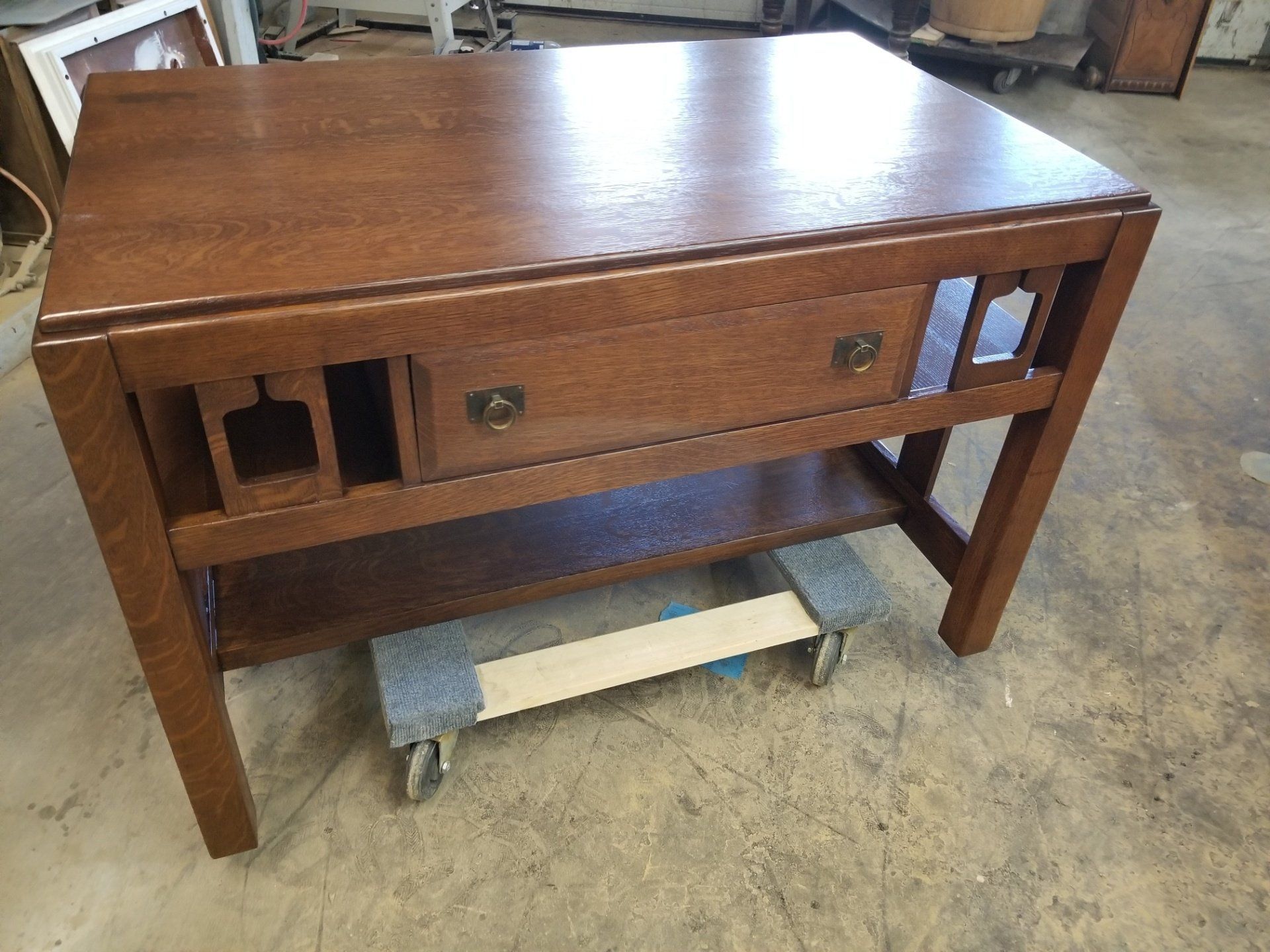 Wooden vintage bench with a drawer and lower shelf, sitting on a concrete floor.