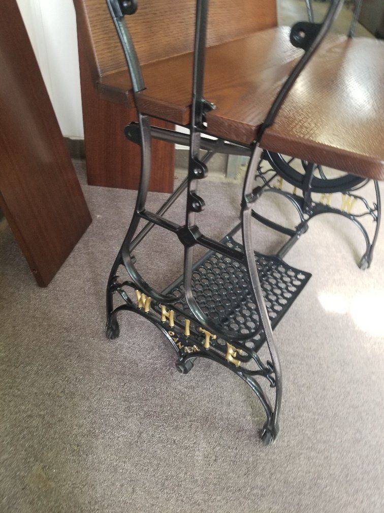 Vintage black metal plant stand beside a wooden table in a carpeted room.