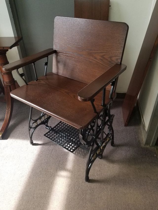 Brown wooden chair with armrests and black wrought-iron base on a carpeted floor.