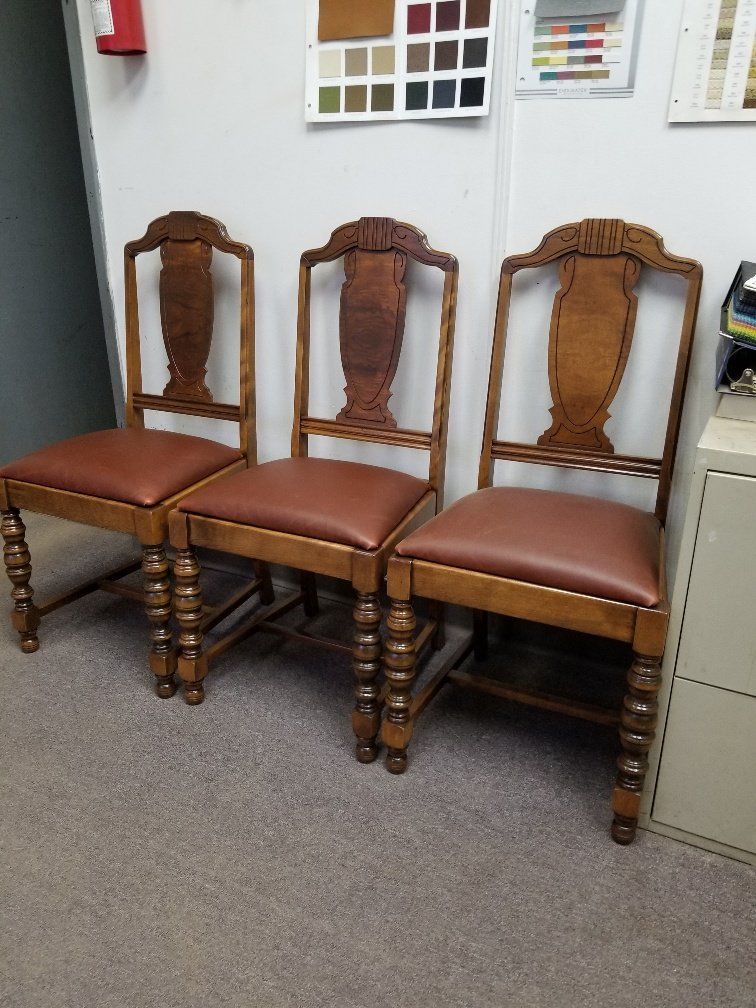 Three wooden dining chairs with brown seats lined up in an office corner